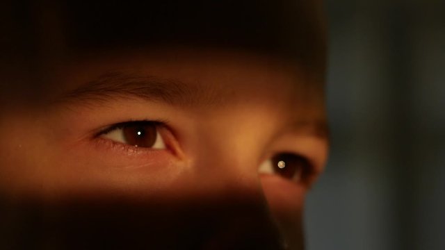 Close up of the brown eyes of a child boy in a strip of light