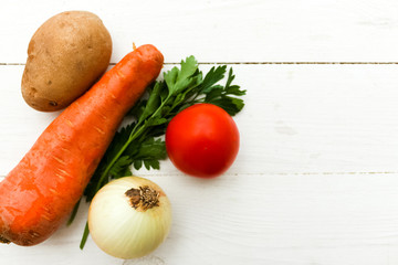 A set of ingredients for soup, carrots, onions, potatoes, tomatoes, against a wood.