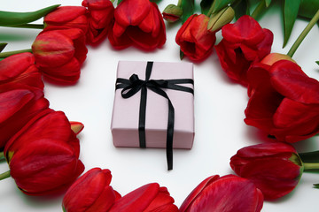 A box with a ribbon is surrounded by tulips.
