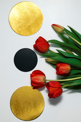Three circles: one black between two gold and a bouquet of tulips on a white background. Flat lay, top view.