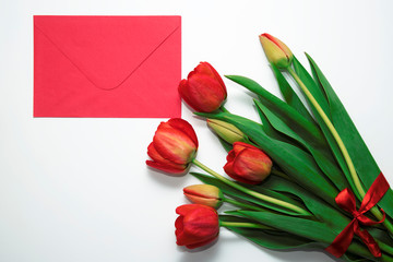 Scarlet envelope and a bouquet of tulips on a white background. Flat lay, top view.