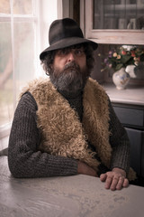 Portrait of a man, a villager, a brunette in a hat and with a beard sits in his home by the window...