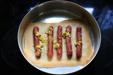 Oven baked crispy hot dog sausages with mustard sauce on baking paper in a baking pan