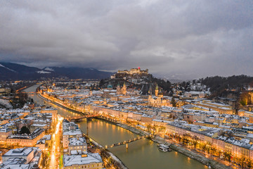 Naklejka premium Aerial drone view of Salzburg snowy old town with city light on at dusk hour in winter