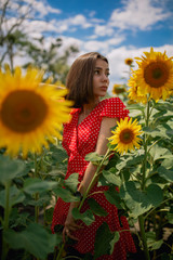 Naklejka premium young beautiful caucasian girl in red dress in white dots stay in sunflower field 