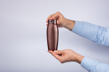 Brown bottle of shampoo or lotion in male hand on white background. Copy space, mock up