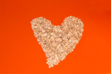 Heart of oatmeal flakes on an orange background. Oatmeal flakes on a bright background. Oatmeal porridge on an orange background. Rolled oats