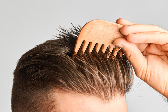 Young man styling his hair with a wooden comb. Hair styling at home. Advertising concept of shampoo for healthy hair and against dandruff. 