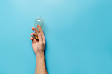 Ecology concept. A man’s hand holds an incandescent lamp on a blue background.