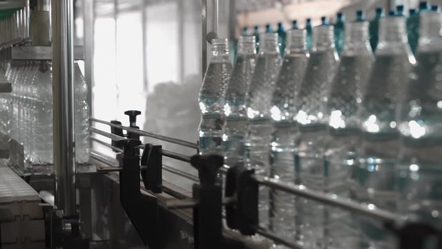 Pure drinking water plant. Work conveyor in the enterprise. Liter bottles on the conveyor are filled with water, closed with lids and glued labels. 4k