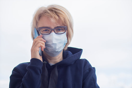 Serious senior woman in protective sterile medical mask on her face calling ambulance, talking on cell mobile phone outdoors. Virus, pandemic coronavirus concept. Covid-19
