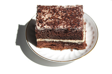 A slice of chocolate cake with white cream with a curl on a light background.