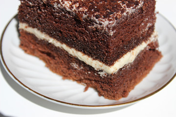 A slice of chocolate cake with white cream with a curl on a light background.
