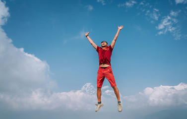 Fototapeta na wymiar Happy man dressed red jumping over the clouds with Annapurna range mountains and Machapuchare 6993m mountain on background as he had trekking to Shanti (Peace) Stupa in Pokhara, Nepal.