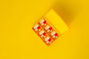 Yellow pillbox with pills on a yellow background