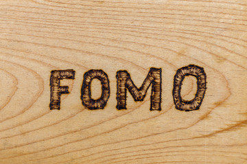 abbreviation FOMO - fear of missing out - burnt by hand on flat wooden surface