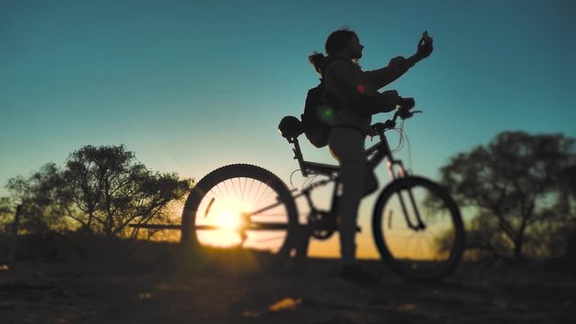 teenage girl photographs herself on a smartphone with a bicycle rides in the park at sunset on nature. healthy girls and lifestyle bike makes selfie