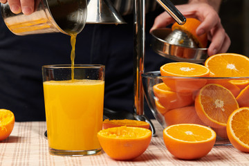 Squeezing an orange with a manual press, close view, making a glass of fresh. Fresh oranges on a wooden table, whole, squeezed and sliced.
