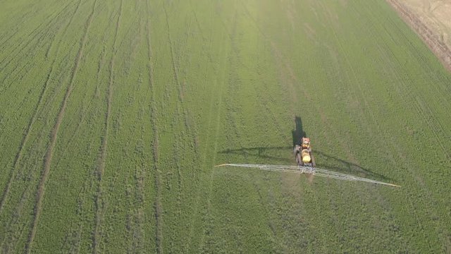 Aerial view of farming tractor spraying on field with sprayer, herbicides and pesticides at sunset. Farm machinery spraying insecticide to the green field, agricultural natural seasonal spring works.