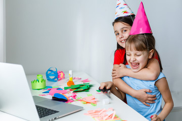 A little girl, curves and laughs in front of a laptop in a cap. Celebrates birthday via internet in...