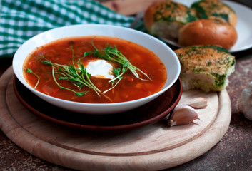 Red borsch with garlic pampusks, peas sprouts and garlic on dark brown background. Traditional dish of ukrainian cuisine. 