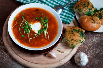 Red borsch with garlic pampusks, peas sprouts and garlic on dark brown background. Traditional dish of ukrainian cuisine. Top view