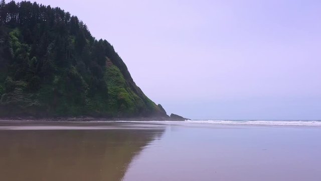 Flying low over Hobbit Beach on the Oregon Coast moving over waves rolling over the sand.