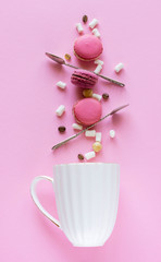 balancing macarons, spoons, marshmallows fly into a white tea mug on a pink background, the concept of balance and harmony