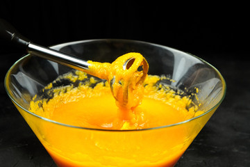 Pumpkin puree with blender in transparent bowl on black background. Cooking mashed pumpkin