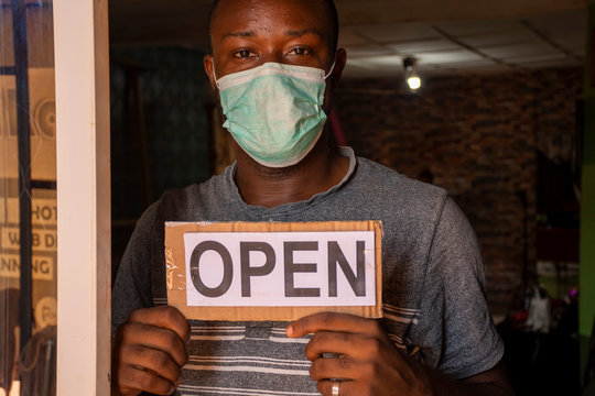 a local african business owner holding open sign standing in front of door