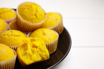 Pumpkin muffins on black plate on white wooden table. Halved cupcake