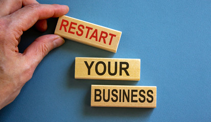 Wooden blocks form the words 'restart your business' on blue background. Male hand.