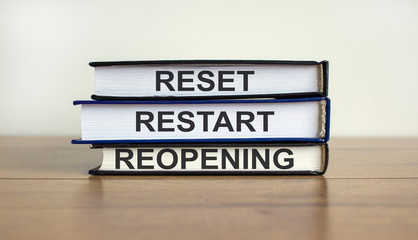Books with text 'reset, restart, reopening' on beautiful wooden table. White background. Business concept.