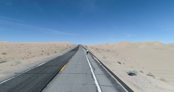 Close tracking shot shows cyclist with sand dunes in the background