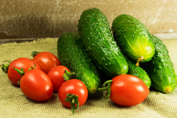 Ripe cherry tomatoes and cucumbers stacked on a tablecloth