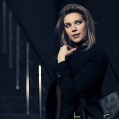 Fashion blonde woman in black coat with handbag