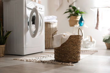 Wicker basket with laundry near washing machine indoors. Interior element