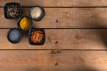 Different kind of Spices in bowls on the left side of a wooden table