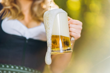 Close-up of the girls hands in dirndl pouring a full glass of beer with huge foam outdoors