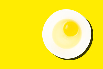 Raw egg in bowl with dark shadow isolated on yellow background. Healthy food and cooking at home concept.