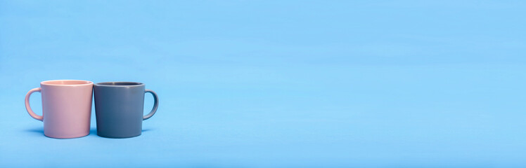 Two beautiful cups of pink and gray are on a blue background. The concept of the holiday is Valentines Day, Mothers Day, International Womens Day. Place for text. Minimalism with coffee. Breakfast