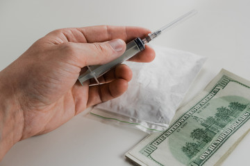 Syringe in hand on a background of money and powdered substance in a package. The concept of drug...