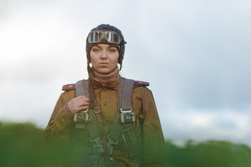 A young female pilot in uniform of Soviet Army pilots during the World War II. Military shirt with shoulder straps of a major, parachute, flight helmet and goggles. © Kozlik_mozlik