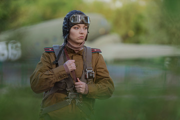A young female pilot in uniform of Soviet Army pilots during the World War II. Military shirt with shoulder straps of a major, parachute, flight helmet and goggles. © Kozlik_mozlik