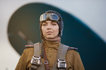 A young female pilot in uniform of Soviet Army pilots during the World War II. Military shirt with shoulder straps of a major, parachute, flight helmet and goggles. © Kozlik_mozlik