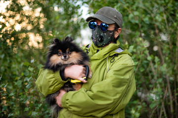 Naklejka na ściany i meble A girl wearing respirator mask walking with Pomeranian dog in the forest protecting from COVID-19.