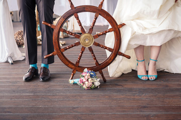 Feet of the bride and groom. Nautical style wedding details. Wooden steering wheel