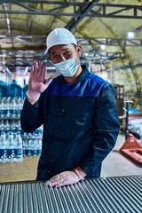 Portrait of a worker in a protective medical mask and a white cap at work behind the conveyor.