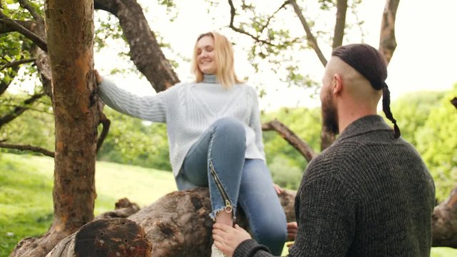A couple is sitting on an old tree branch. The woman and man are appreciating each other and smiling. The happy lovers are alone in nature.