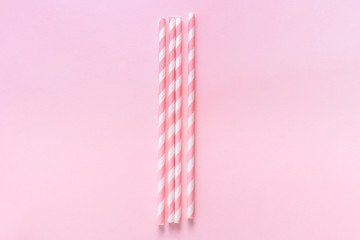Pastel paper straws with white stripes on soft pink background. Zero waste party concept. Flat lay...
